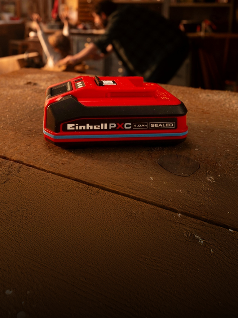 Einhell Power X-Change 4,0 Ah SEALEAD-batteri på en arbejdsbænk af træ med blå ring og synlig etiket.