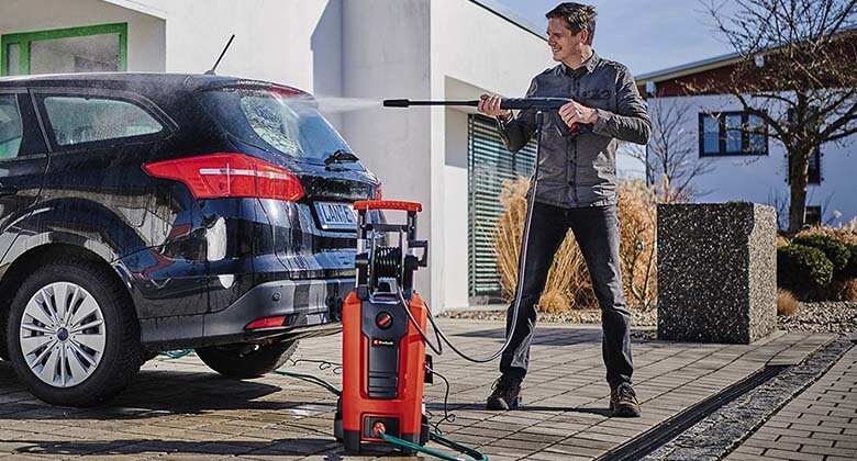 Mand, der rengør bilen med højtryksrenser.
